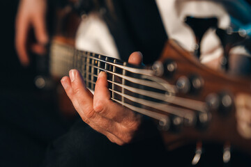 Closeup of male fingers playing the fretboard of a 5 stringed bass guitar