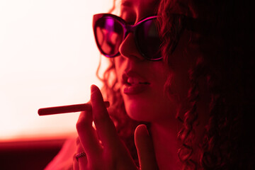 Obraz premium chica con un cigarro en la mano y gafas de sol en el coche con tonos rojos