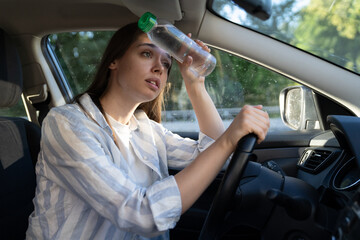 Exhausted woman driver feeling headache, sitting inside her car, applies bottle of water to forehead, hot weather. Tired girl stop after driving car in traffic jam. Blood pressure, heat concept. 