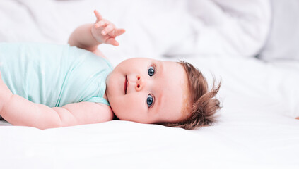 A newborn baby is lying on a snow-white bed. A beautiful child of European appearance. Healthy sleep, wakefulness, and waking up in the morning.