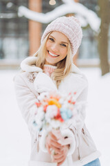 Young woman in winter clothes walks in the park holding a delicate bouquet of dried flowers.