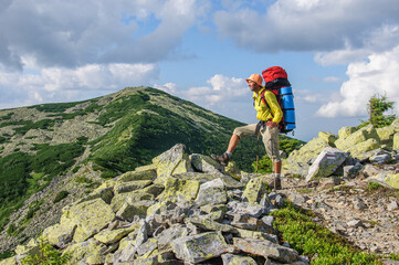 A male tourist with a large backpack climbs a mountain stone path high in the Carpathian Gorgan. Ukraine