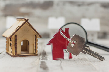 Metal keyring in the shape of a house with a metal key under a magnifying glass on a white wood plank background. Real estate concept