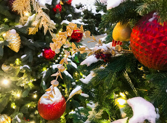 True Christmas background: green branches of a Christmas tree covered with snow, with lights and glass decorations with toys, balls and figures of red and gold color. Copy space