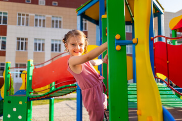 a happy child girl plays at the children's complex playground near the house in the summer in the yard and smiles
