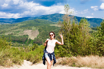 Fototapeta na wymiar Young smiling woman tourist showing victory sign on the top of the mountain. Hiking concept. Vacation in the mountains.