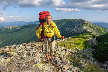 A male tourist with a large backpack climbs a mountain stone path high in the Carpathian Gorgan. Ukraine