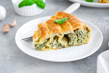 Greek pie spanakopita with feta cheese and spinach on a white plate on a gray concrete background. Copy space.