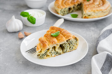 Greek pie spanakopita with feta cheese and spinach on a white plate on a gray concrete background. Copy space.