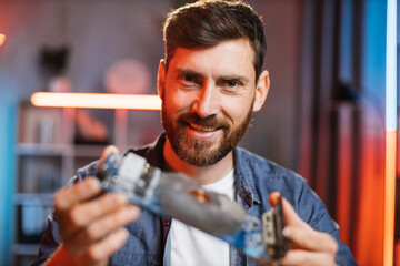 Close up of satisfied smiling bearded man sitting at table and showing repaired graphics card from...