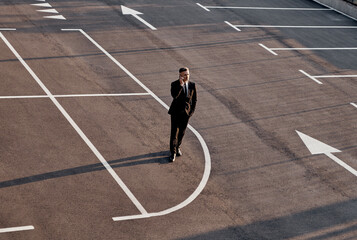 Top view of man in formalwear talking on mobile phone while standing on parking lot with arrow sign...