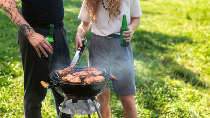 Young couple frying meat on the grill and drinking beer