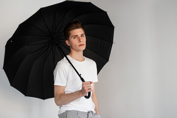 Fashion model handsome young man in youth fashionable T-shirt stands with vintage umbrella near...