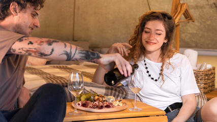A happy couple resting in a tent at glamping. Wine and food © frimufilms