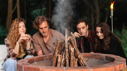 A group of happy young friends trying to make a campfire at glamping