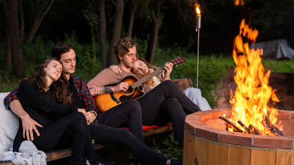 A group of happy young friends near a campfire at glamping