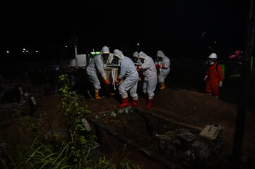 group of people bringing coffin of covid19 victim to the grave pit for funeral at night