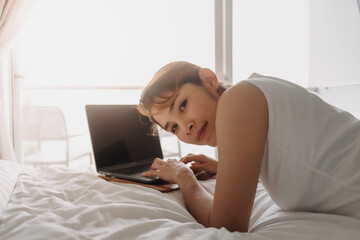 Asian woman works with laptop on the bed. Concept of work from hotel.