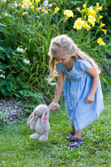 Selective focus vertical full length portrait of cute little girl standing in a park alley walking her plush bunny toy