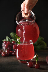 Pouring red cherry compote in glass on black background. Vertical format.