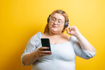 Young plus size Caucasian model listening to music with headphones from her mobile phone
