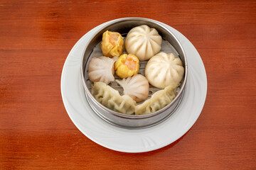 Chinese dim sum and assorted Japanese gyozas steamed in characteristic metal container on white plate