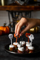 Obraz na płótnie Canvas Sweet Halloween treat, chocolate covered marshmallows with sugar and Halloween decorations on a black plate, vertical photo with soft focus