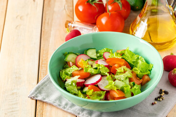 Fresh vegetable salad with olive oil in ceramic bowl on wooden background. Seasonal summer dish of tomatoes, cucumbers and radishes.