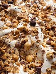 Hazelnut flavour gelato - full frame detail. Close up of a beige surface texture of Ice cream covered with pieces of hazelnuts.