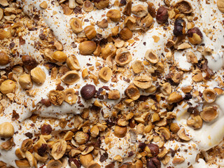 Hazelnut flavour gelato - full frame detail. Close up of a beige surface texture of Ice cream covered with pieces of hazelnuts.