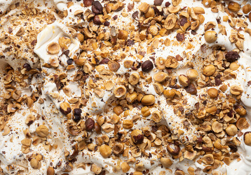 Hazelnut Flavour Gelato - Full Frame Detail. Close Up Of A Beige Surface Texture Of Ice Cream Covered With Pieces Of Hazelnuts.