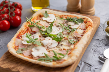 Rectangular pizza with mushrooms, tomatoes and arugula on a wooden cutting board