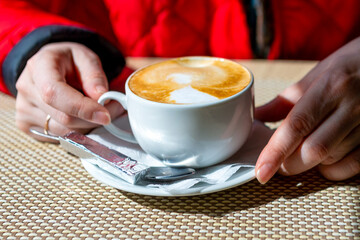 A cup of aromatic latte coffee stands on the cafe table on a bright sunny morning.