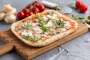 Rectangular pizza with mushrooms, tomatoes and arugula on a wooden cutting board