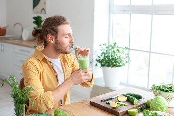 Young man drinking healthy green smoothie in kitchen