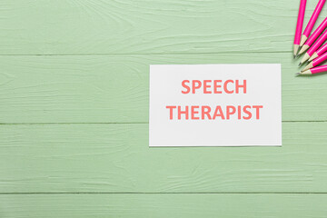 Paper with text SPEECH THERAPIST and pencils on color wooden background