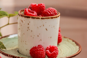 Fresh ripe red raspberries in a cup on a green saucer.