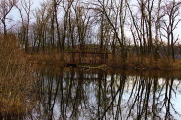 Obraz premium Abandoned ruins skeleton of barge near the shore of lake. Bare trees in the background. Trees reflected in tranquil water. Concept of landscape and nature