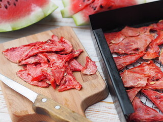 Dried and fresh slices of watermelon on the kitchen board against the grates from the watermelon dryer.