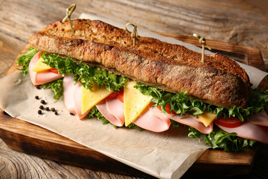Board with tasty ciabatta sandwich on wooden background, closeup