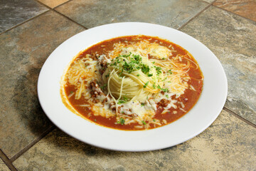 Angel Hair Bolognese, dish of vegetable and meat soup with noodles in white bowl on tiles