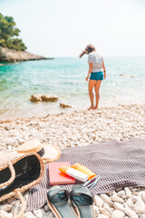 young pretty woman in summer outfit walking by sea shore blanket with beach stuff on blanket