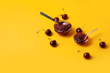 Bowls of tasty cherry jam on color background