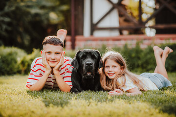  girl and teen boy laying on green grass with black Labrador retriever.