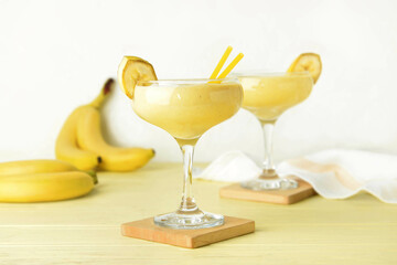 Glasses of tasty banana daiquiri cocktail and fruits on light background
