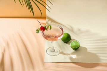 Glass of tasty cosmopolitan cocktail and limes on color background