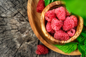 Fresh juicy raspberries in wooden bowl. Summer still life with raspberries on an old wooden table. Copy space .Jar of raspberry jam and fresh berries on wooden background