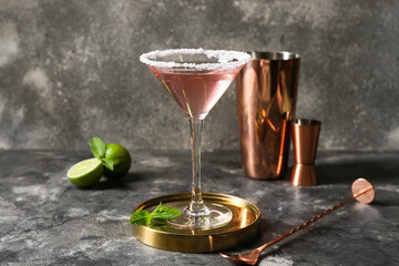 Glass of tasty cosmopolitan cocktail, spoon and shaker on dark background