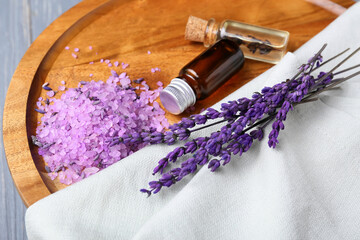 Fototapeta na wymiar Tray with bottles of lavender essential oil, sea salt and flowers on table