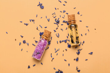 Bottles of lavender essential oil and flowers on color background